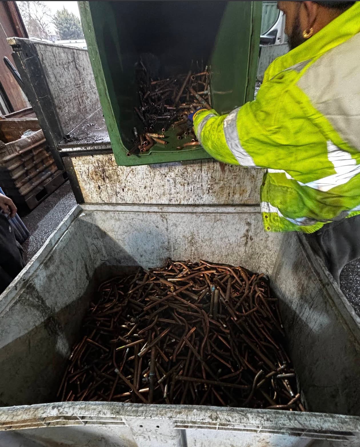 A Foremost Metal Recycling operative in hi-vis tipping a bin of copper pipe offcuts into a steel stillage at the Egham site